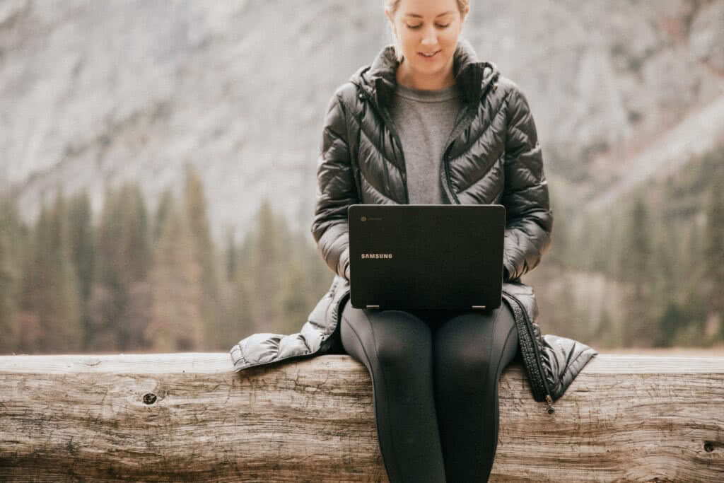 Eine Frau in Sportkleidung sitzt mit einem Laptop in der Natur